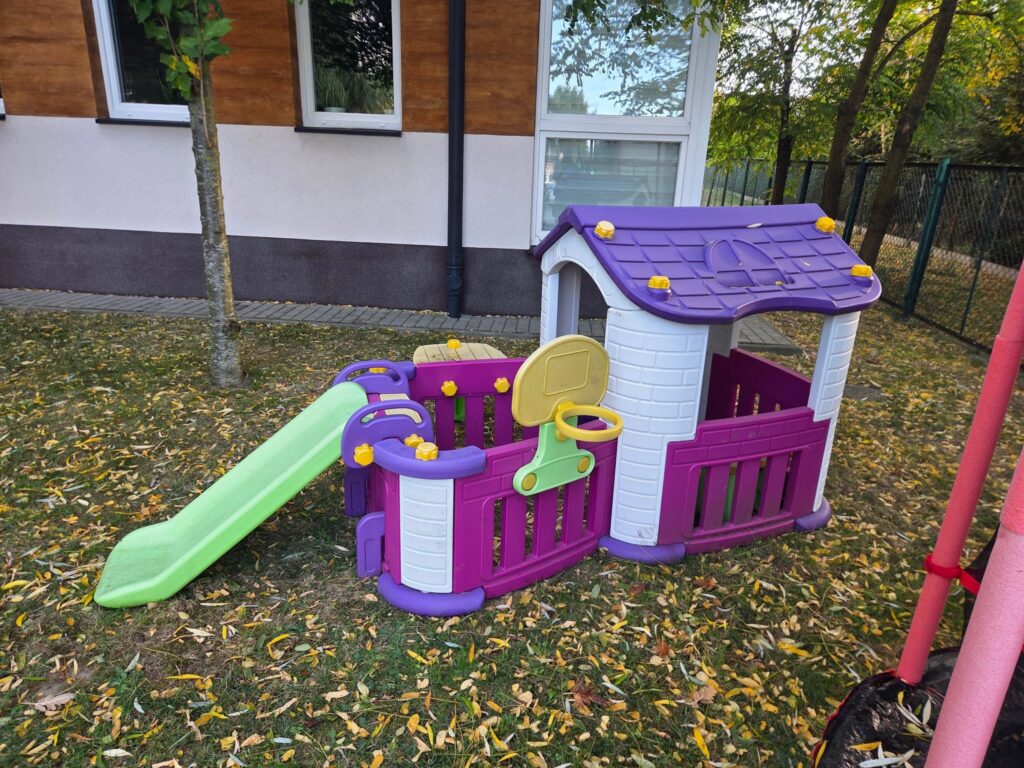 Pusty ogród żłobka z domkiem, zjeżdżalnią i jesiennymi liśćmi